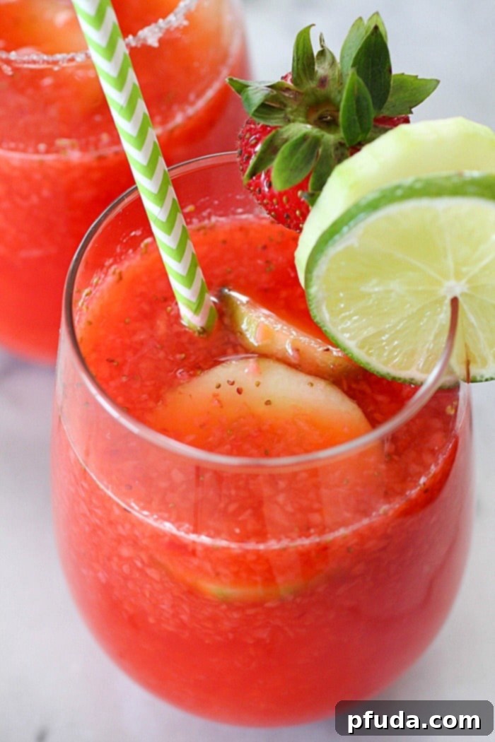 A refreshing glass of strawberry limeade garnished with cucumber slices and a lime wedge, sitting on a wooden surface, embodying the perfect cool-down drink.