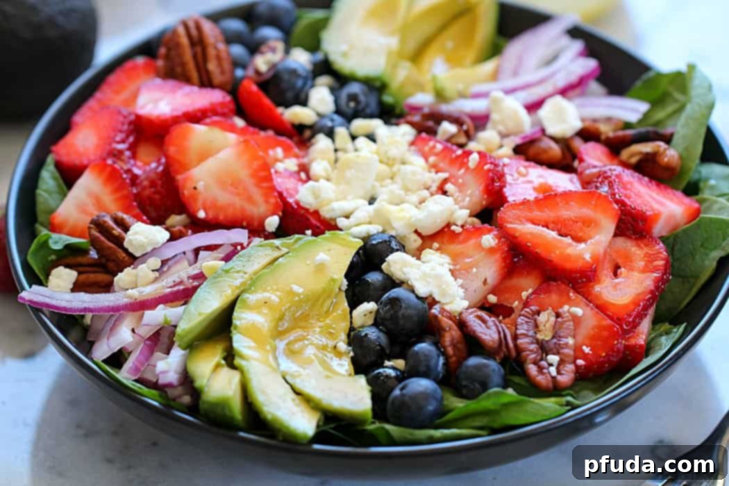 Vibrant spinach salad with fresh berries, sliced California avocado, feta, red onion, and walnuts, drizzled with honey-garlic vinaigrette. A perfect healthy meal.