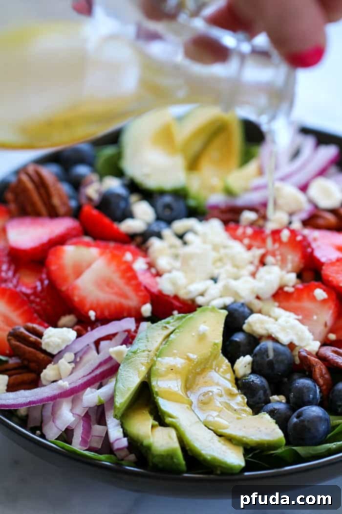 Close-up of a refreshing summer spinach salad with colorful berries, creamy California avocado slices, crumbled feta cheese, and crunchy walnuts, ready to be dressed.