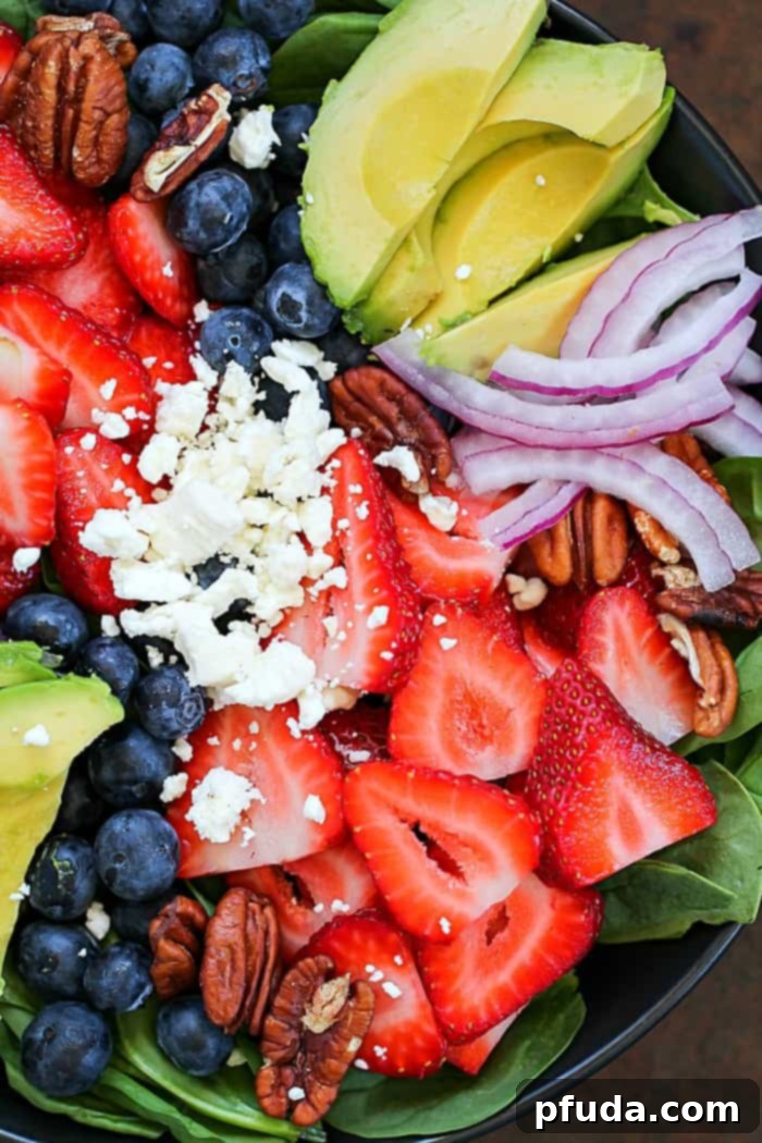 A close-up shot of a gourmet spinach salad packed with colorful berries, creamy California avocado, crumbled feta cheese, and crunchy walnuts, showcasing its delicious texture.