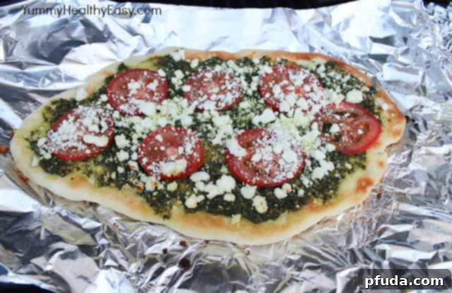 A freshly sliced grilled pesto pizza with melted goat cheese and tomatoes, ready to be served.