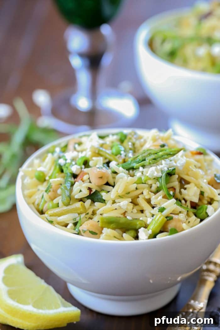 Close up view of a beautiful salad filled with orzo, asparagus, toasted almonds, arugula, feta cheese and peas with a vinaigrette.