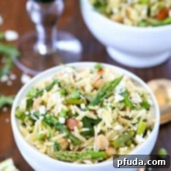Top view of a beautiful Spring Orzo Salad filled with orzo, asparagus, toasted almonds, arugula, feta cheese and peas with a vinaigrette.