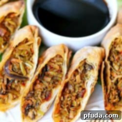 Crispy Air Fryer Vegetable Egg Rolls 3 White plate with egg rolls sliced in half, surrounding a bowl of soy sauce.
