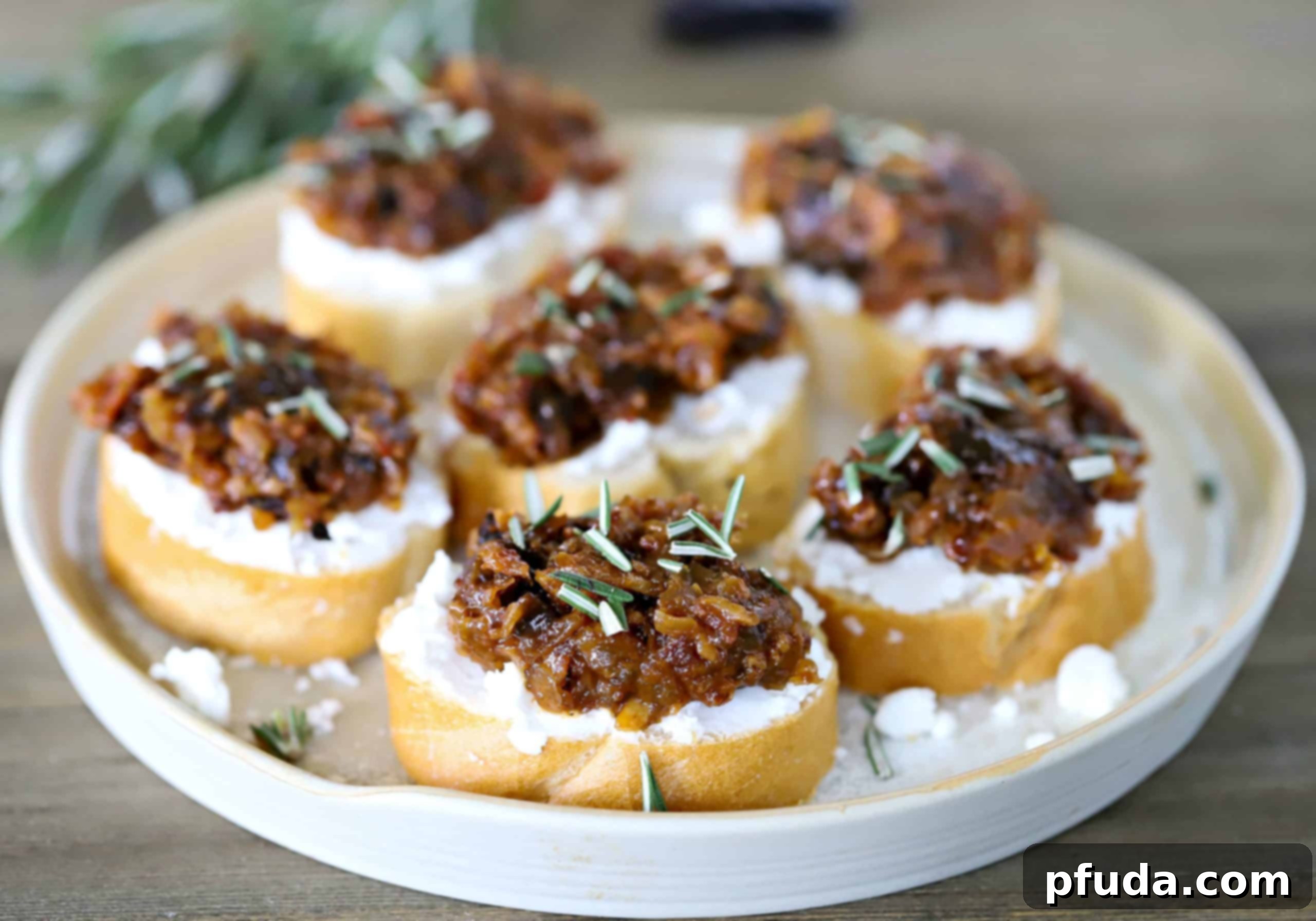 Elegant white plate filled with golden-brown Prune Bacon Jam Crostini, garnished with fresh rosemary.