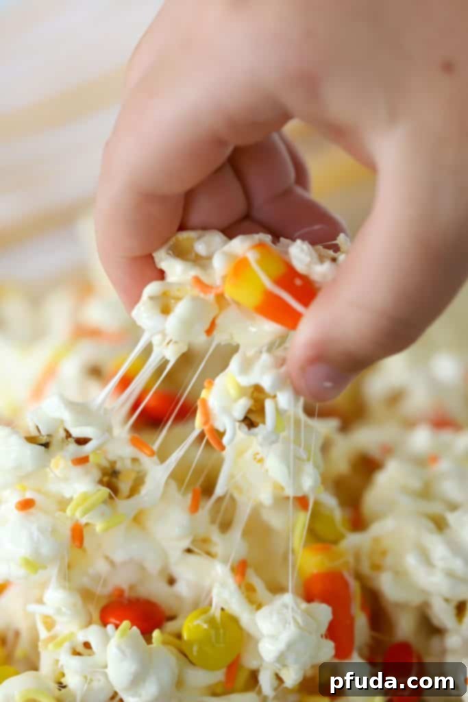 No Bake Candy Corn Popcorn Clusters 4 Gooey Marshmallow Popcorn Treat being pulled from a bowl, highlighting its texture