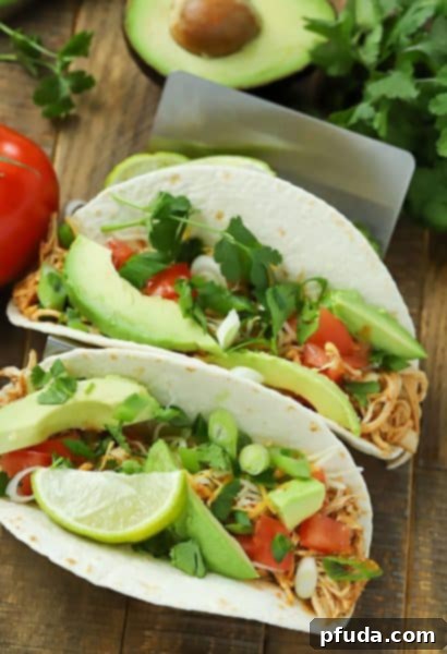 Easy Slow Cooker Low-Sodium Shredded Taco Chicken 2 Two taco shells filled with slow cooker taco chicken and topped with avocado, tomato, and green onions.