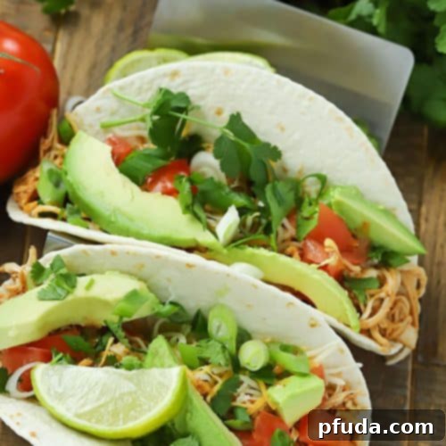 Easy Slow Cooker Low-Sodium Shredded Taco Chicken 8 Two taco shells filled with slow cooker taco chicken and topped with avocado, tomato and green onions.