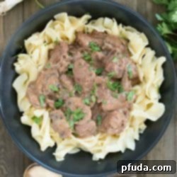 Black plate filled with egg noodles and topped with beef stroganoff. Square overhead picture.
