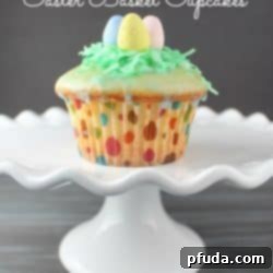 Vanilla Glazed Easter Basket Cupcakes featuring blue glaze, green coconut, and speckled candy eggs.
