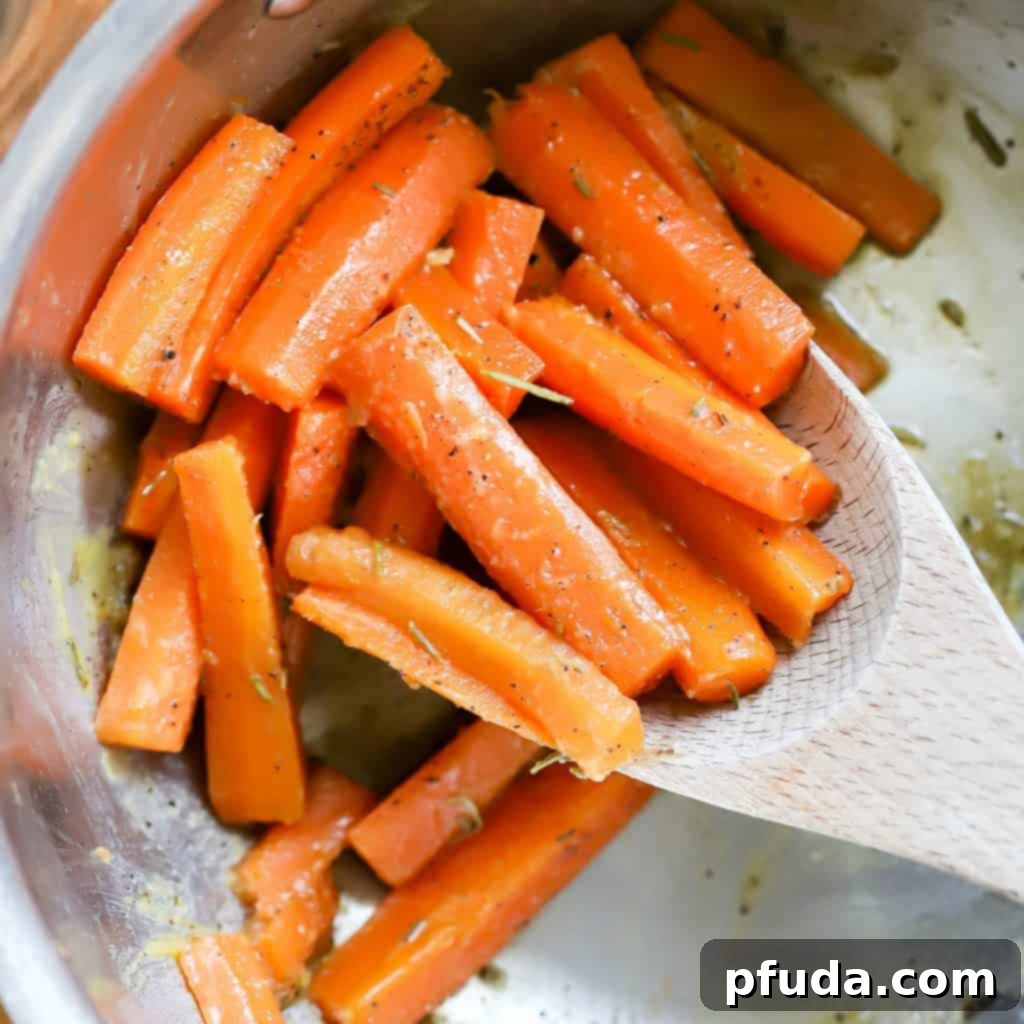 A large pan filled with vibrant, cooked glazed carrots and a wooden spoon, showcasing their perfect tenderness.