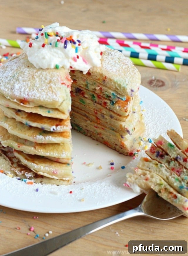 A stack of fluffy Funfetti Pancakes with a small hand reaching for them.