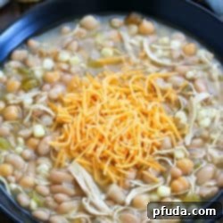 Black bowl filled with white chicken chili and topped with shredded cheese.