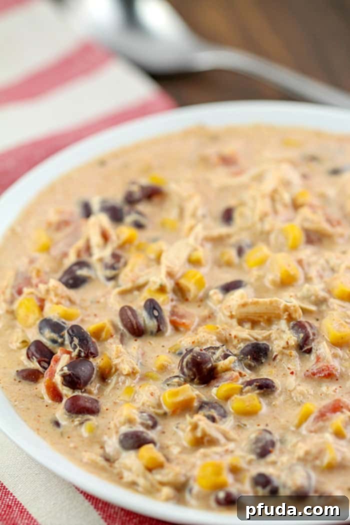 Ultimate Easy Crock Pot Cream Cheese Chicken Chili 3 A bowl of creamy Crock Pot Cream Cheese Chicken Chili with tortilla chips and a spoon.