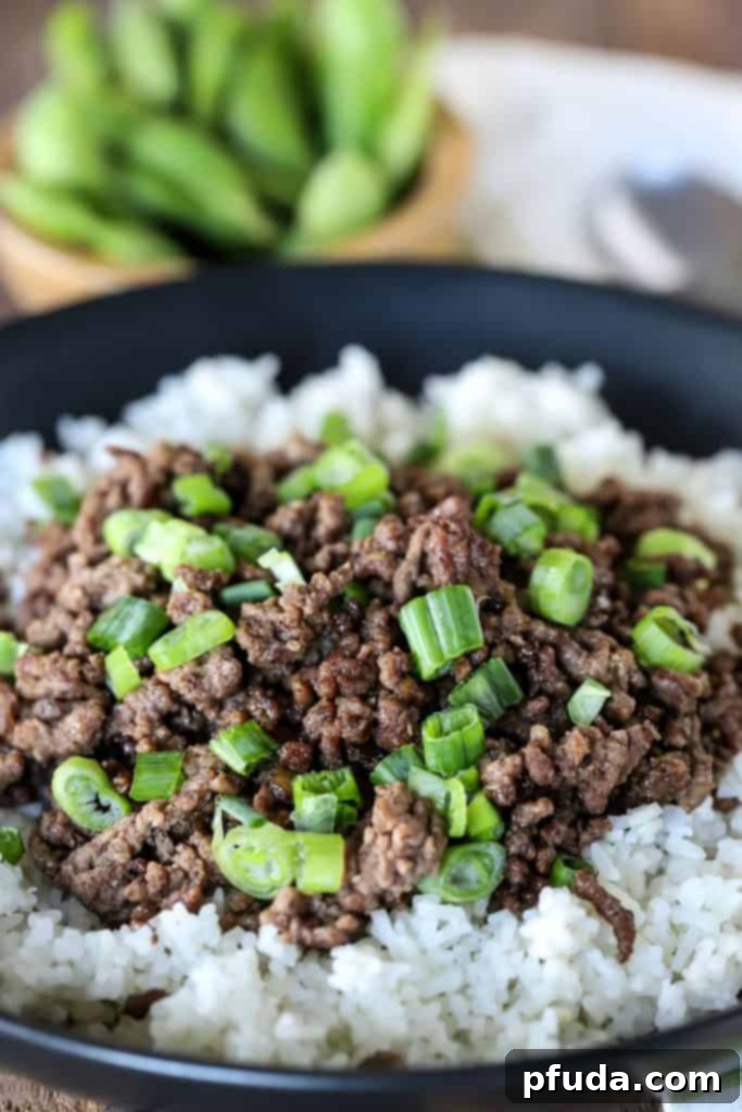 A plate of Korean beef on a bed of white rice, topped with chopped green onions.