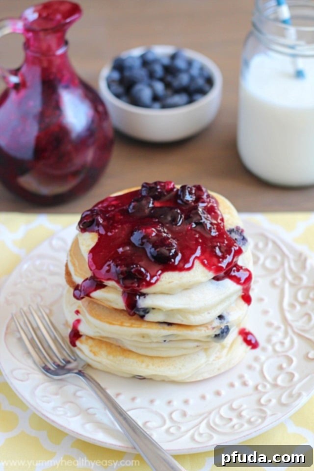 Closeup shot of a stack of blueberry pancakes being drizzled with homemade blueberry syrup