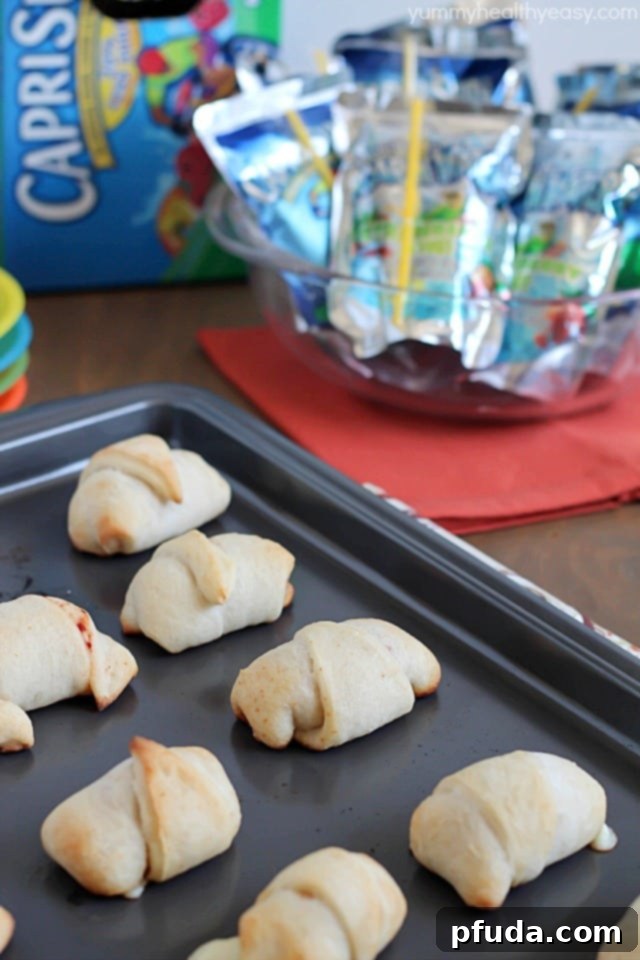 A close-up of freshly baked pepperoni and cheese pizza rolls, perfectly golden brown, served alongside a colorful array of Capri Sun juice pouches, highlighting the ideal pairing for kids.