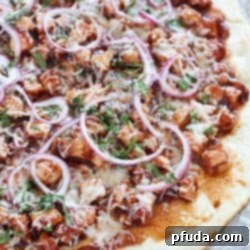 Homemade Grilled BBQ Chicken Pizza with a no-rise homemade crust and topped with grilled chicken, BBQ sauce, red onion, cilantro & mozzarella on a piece of parchment paper.