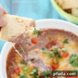 A golden pita chip delves into a bowl of rich, cheesy Healthy Black Bean Dip, a perfect snack or party appetizer.