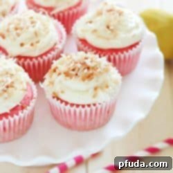 A tray of vibrant strawberry soda cupcakes with creamy lemon frosting and coconut flakes.