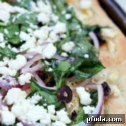 Easy Greek Pizza Recipe with a mayo & garlic spread and topped with feta, red onion, spinach, sun dried tomatoes and kalamata olives. Crazy delicious!