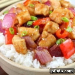 A close-up shot of a white bowl filled with Orange Chicken Stir Fry, garnished with green onions and sesame seeds, with chopsticks resting on the side.