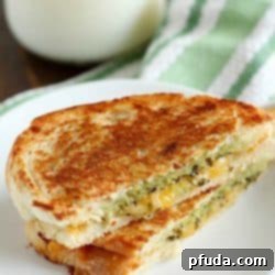 Pesto Grilled Cheese Panini cut in half on a white plate with a glass of milk in the background.